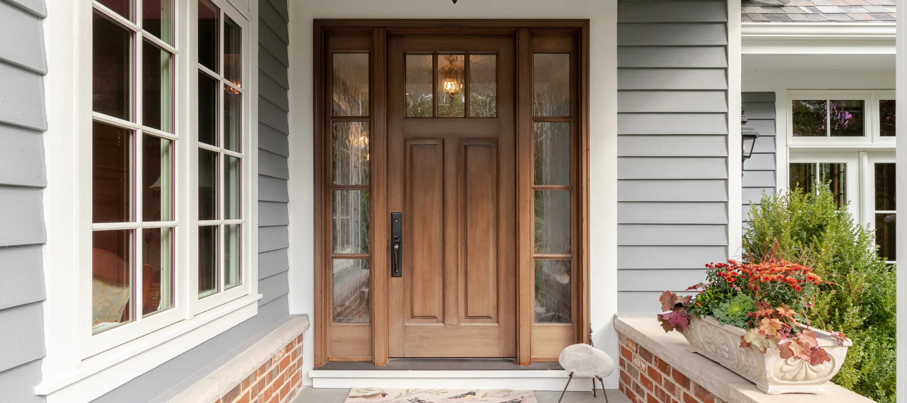 Elegant wooden front door with glass side panels and gray siding