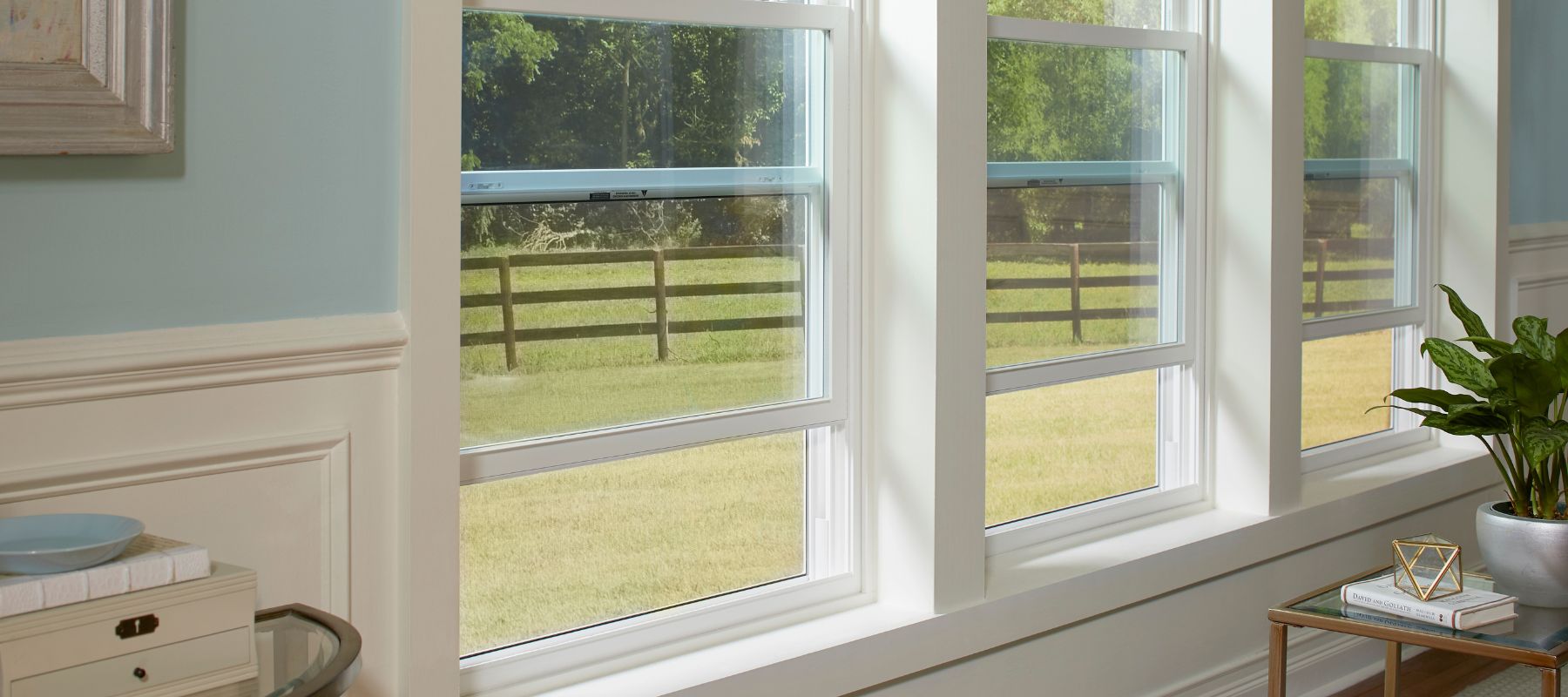 Series of white-framed double-hung windows letting in natural light in a cozy living space with light blue walls
